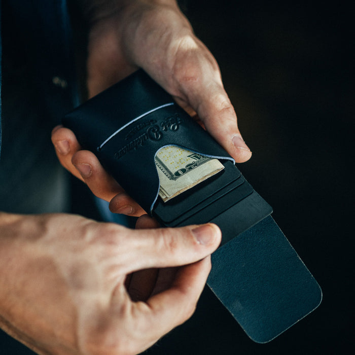 Person holding a black leather wallet with money sticking out, against a dark background