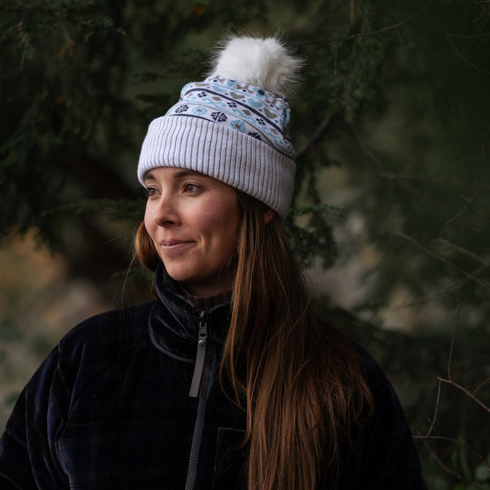 Woman wearing a white beanie with a pom-pom in a forest setting