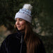 Woman wearing a white beanie with a pom-pom in a forest setting