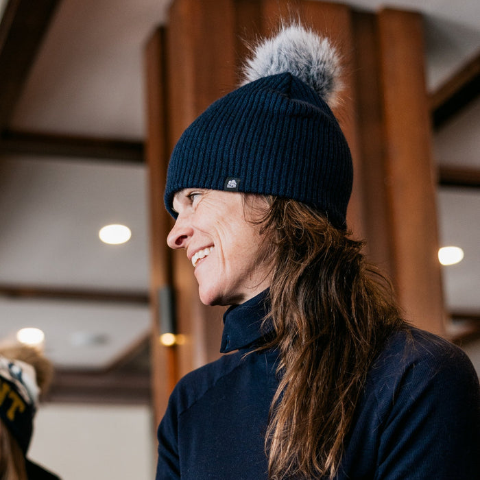 Person wearing a dark blue knit hat with a pom-pom indoors