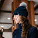 Person wearing a dark blue knit hat with a pom-pom indoors