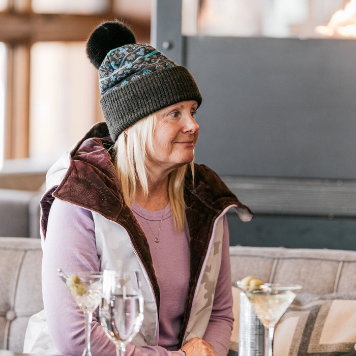 Woman in a cozy setting wearing a winter hat and coat, sitting at a table with drinks.