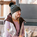 Woman in a cozy setting wearing a winter hat and coat, sitting at a table with drinks.