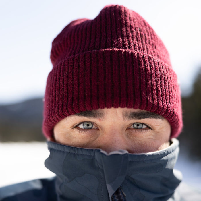 Person wearing a red knit beanie and dark jacket in a snowy landscape