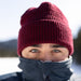 Person wearing a red knit beanie and dark jacket in a snowy landscape