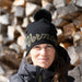 Person wearing a black beanie with 'Vermont' text in front of stacked firewood.