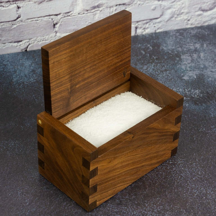 Wooden salt cellar with salt on a dark surface with a brick wall background
