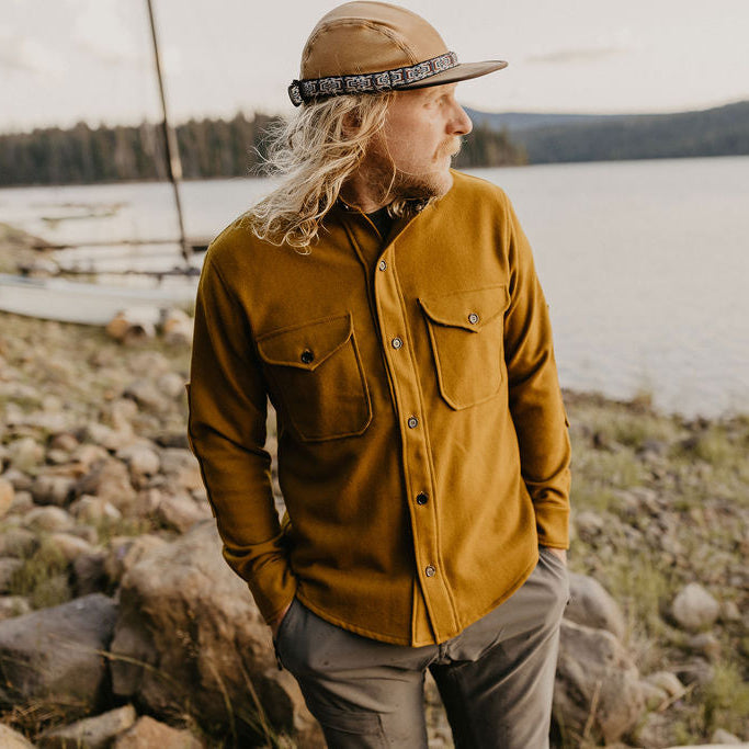 Man wearing a mustard yellow shirt and brown cap by a lake