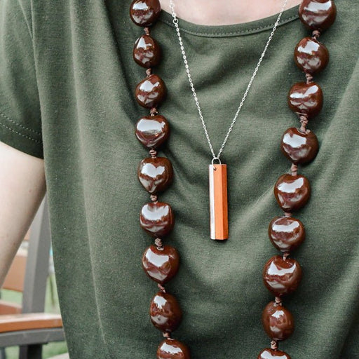 Person wearing a long brown beaded necklace with a pendant on a green shirt.