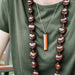Person wearing a long brown beaded necklace with a pendant on a green shirt.