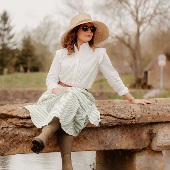Woman in a white blouse and green skirt sitting on a stone wall outdoors.