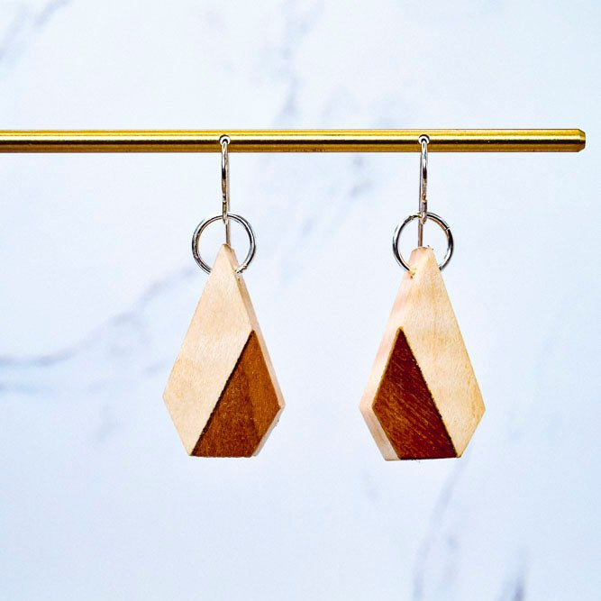 Wooden geometric earrings on a gold bar against a light blue background