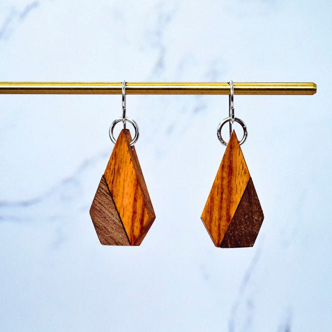 Wooden geometric earrings on a gold rod against a marble background