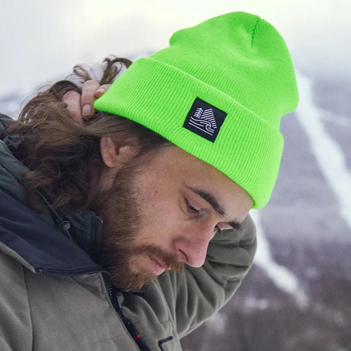 Person wearing a bright green beanie with a logo, standing against a snowy landscape.