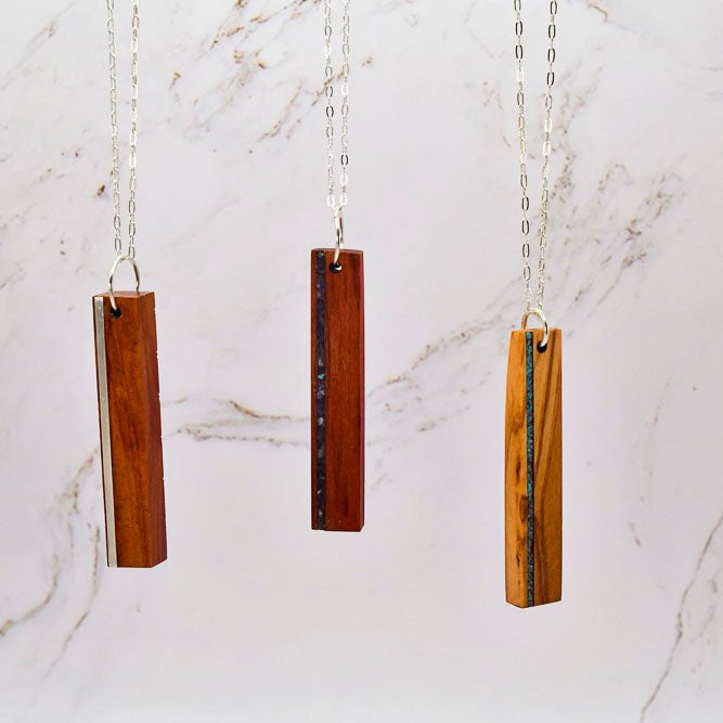 Three wooden pendant necklaces on silver chains against a marble background