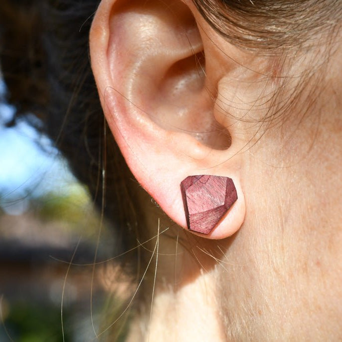 Close-up of an ear wearing a purple geometric earring with a blurred outdoor background
