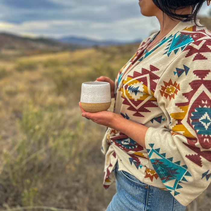 Person holding a ceramic cup in a scenic outdoor setting