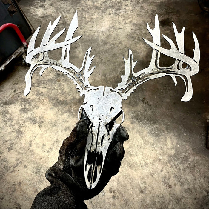 Metallic deer skull with antlers held by a gloved hand on a concrete floor.